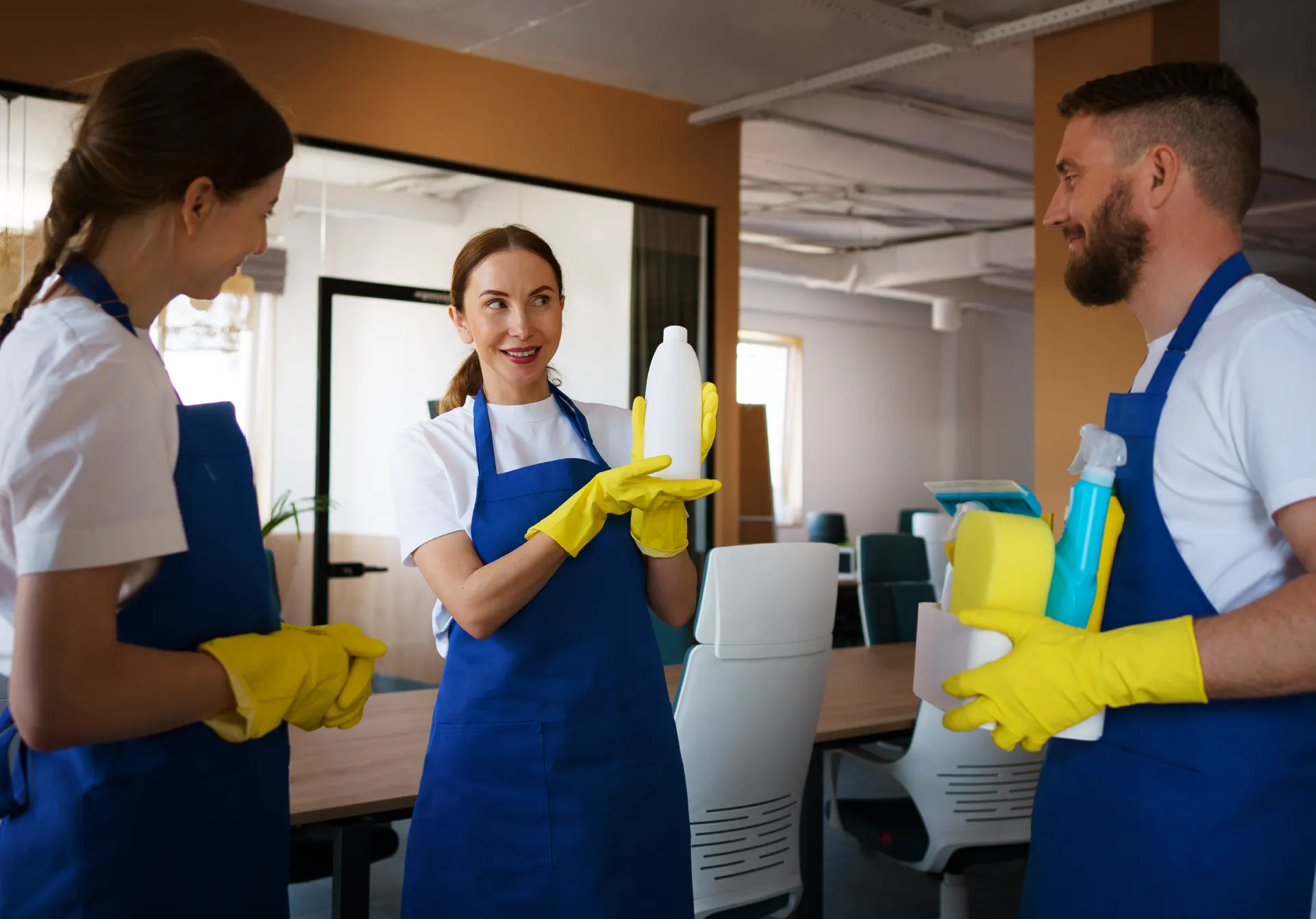Tres trabajadores de limpieza con delantales azules y guantes mostrando un producto en una oficina